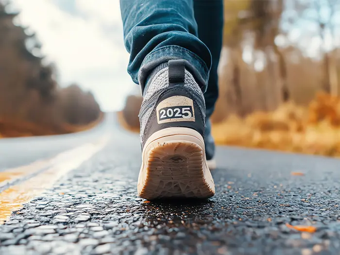 Close up of legs walking on a road, back of trainer labelled with 2025