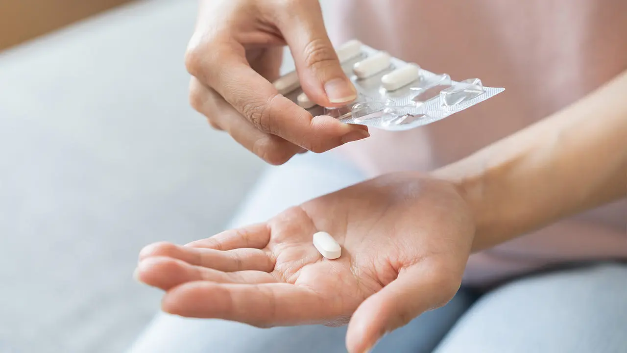 Close-up of a person opening a medical blister pack, dispensing a pill in the palm of their hand.