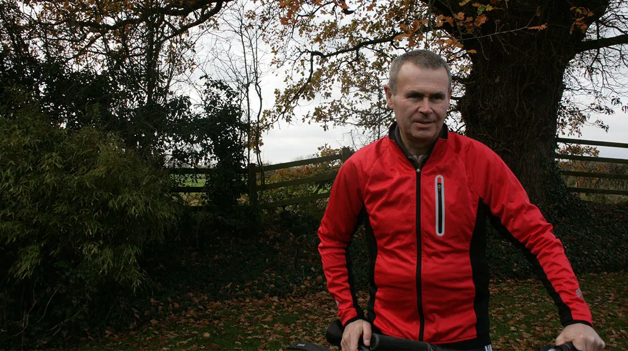 Picture on Stephen outside riding his bike, in the country side with trees and bushes around him