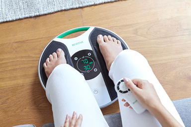 Image of womans legs, with her feet on the medic device with the remote control in her hand 