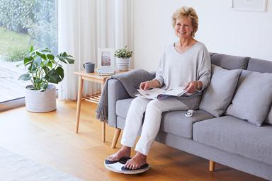  Image of a lady in her lounge sitting on a sofa with her feet on a medic device 