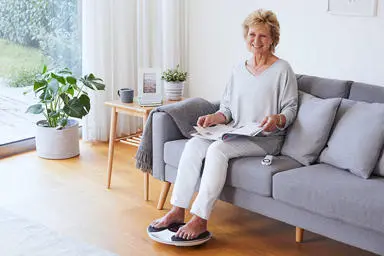  Image of a lady in her lounge sitting on a sofa with her feet on a medic device 