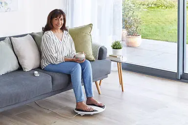 Image of a lady in her lounge sitting on a sofa with her feet on a prohealth device 